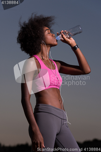 Image of african american woman drinking water after jogging in nature