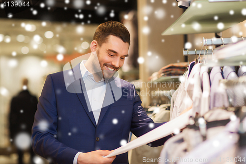 Image of happy young man choosing clothes in clothing store