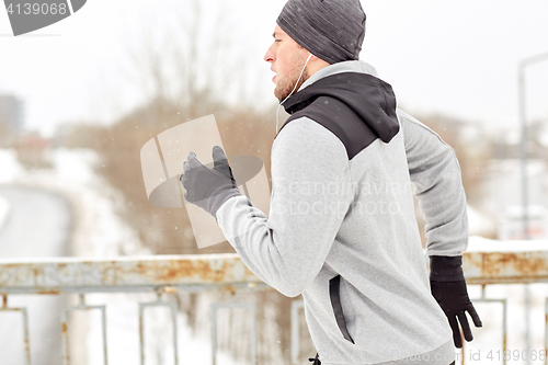 Image of man in earphones running along winter bridge