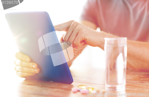 Image of close up of hands with tablet pc, pills and water