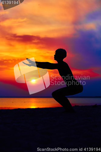 Image of Silhouette of woman standing at yoga pose on the beach during an amazing sunset