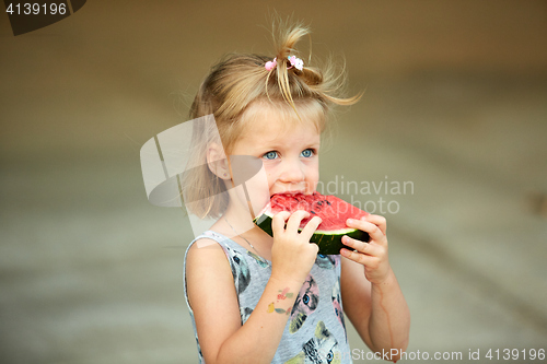 Image of Adorable blonde girl eats a slice of watermelon outdoors.