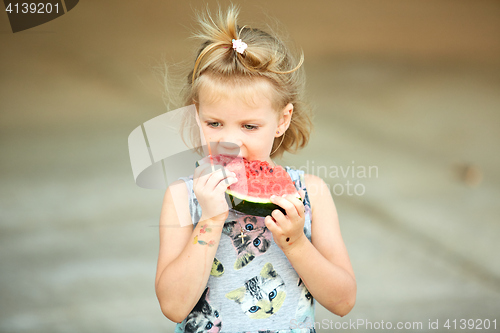 Image of Adorable blonde girl eats a slice of watermelon outdoors.