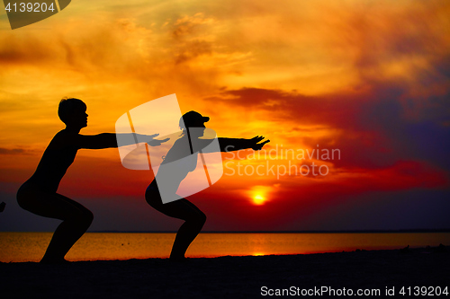 Image of Yoga people training and meditating in warrior pose outside by beach at sunrise or sunset.