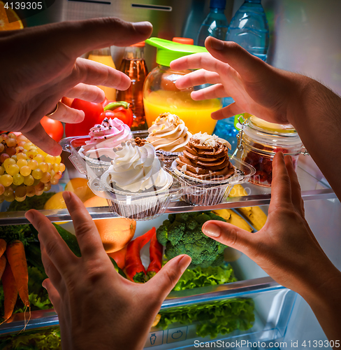 Image of Human hands reaching for sweet cake at night in the open refrige