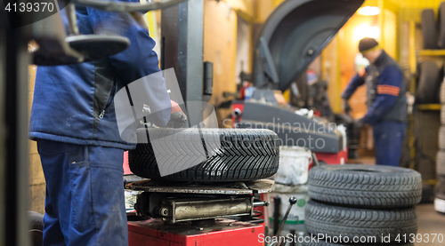 Image of Professional auto mechanic replacing tire on wheel in car repair service.