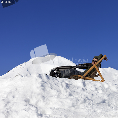 Image of Skier at winter mountains resting on sun-lounger in outdoor cafe