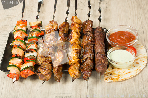 Image of set shashlik. kebab skewer, black rectangular plate. sauce and onions