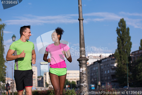 Image of young smiling multiethnic couple jogging in the city