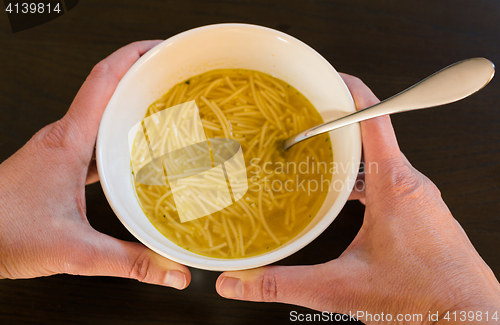 Image of Female hands holding a bowl with European noodle soup