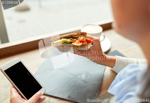 Image of woman with smartphone and sandwich at restaurant