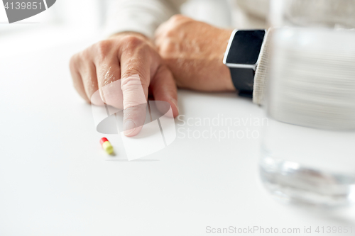 Image of close up of old man hand with pill and smart watch