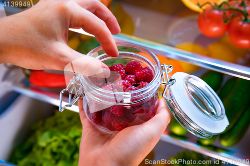 Image of Woman takes the fresh raspberries from the open refrigerator