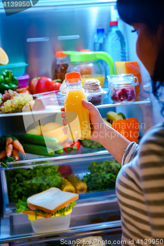 Image of Woman takes the Orange juice from the open refrigerator