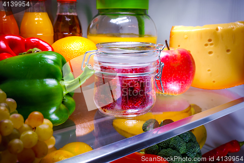 Image of Fresh raspberries in a glass jar on a shelf open refrigerator