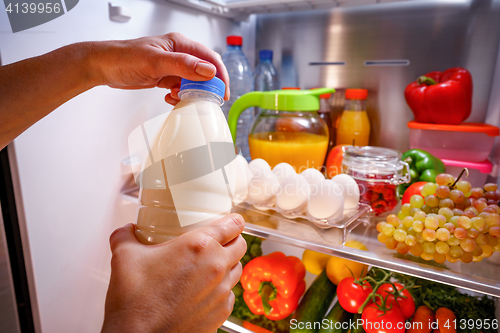 Image of Woman takes the milk from the open refrigerator