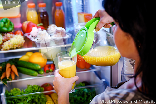 Image of Woman takes the Orange juice from the open refrigerator