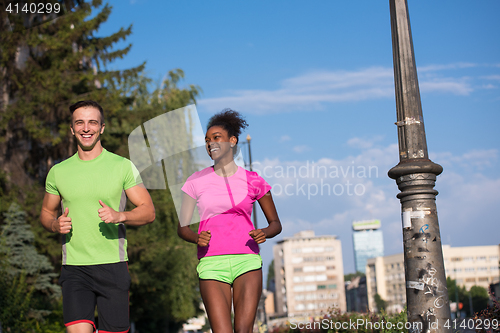 Image of young smiling multiethnic couple jogging in the city