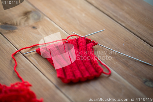 Image of hand-knitted item with knitting needles on wood