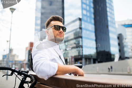 Image of happy young man with bicycle sitting on city bench