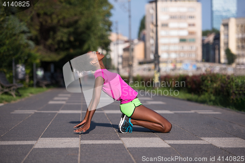 Image of sporty young african american woman stretching outdoors