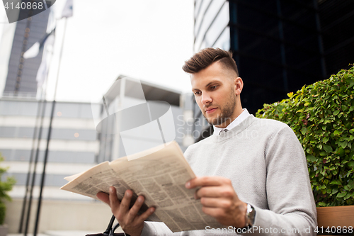 Image of man reading newspaper on city street bench