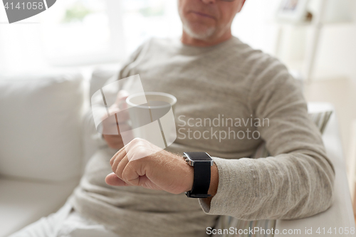 Image of close up of old man with mug looking at wristwatch