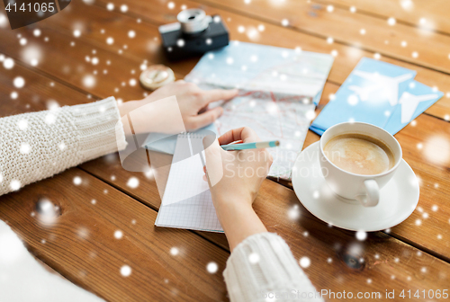 Image of hands with map and coffee writing to notebook