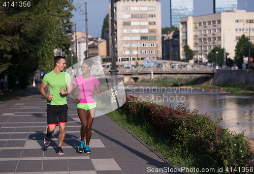 Image of young smiling multiethnic couple jogging in the city