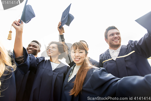 Image of happy students or bachelors waving mortar boards