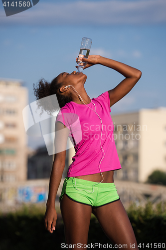 Image of african american woman drinking water after jogging
