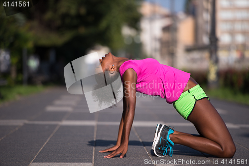 Image of sporty young african american woman stretching outdoors