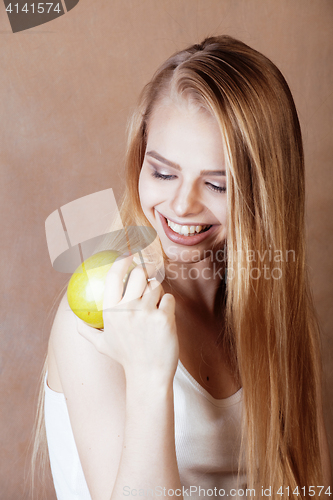 Image of young pretty blond woman with green apple happy cheerful smiling close up on warm brown background, lifestyle people concept