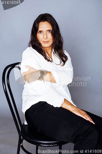 Image of pretty brunette confident mature woman sitting on chair in studi