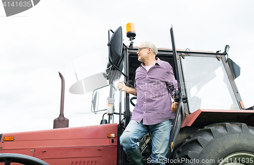 Image of old man or farmer getting out of tractor at farm