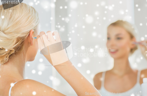 Image of woman cleaning ear with cotton swab at bathroom