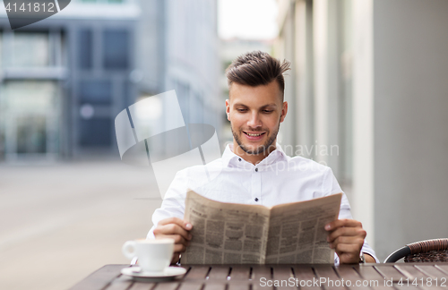 Image of smiling man reading newspaper at city street cafe
