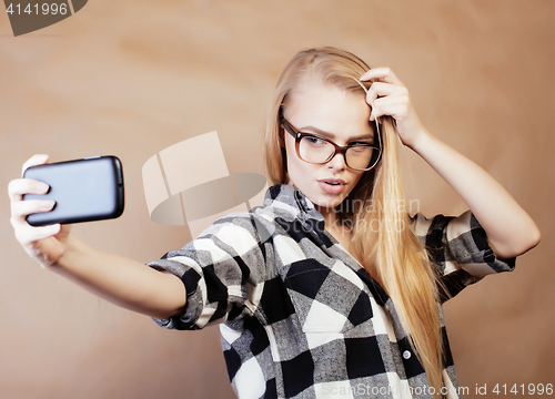 Image of young pretty blond hipster girl making selfie on warm brown background, lifestyle people concept