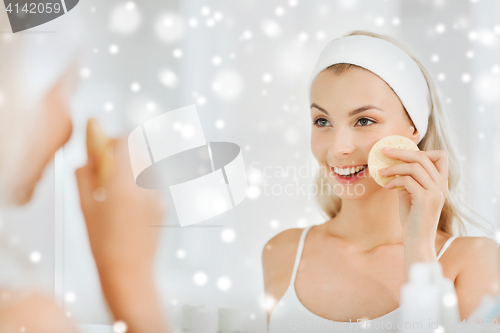 Image of young woman washing face with sponge at bathroom