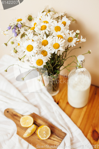 Image of Simply stylish wooden kitchen with bottle of milk and glass on table, summer flowers camomile, healthy foog moring concept