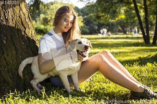 Image of young attractive blond woman playing with her dog in green park at summer, lifestyle people concept