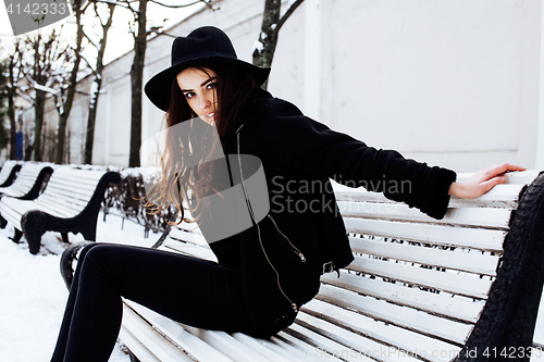 Image of young pretty modern hipster girl waiting on bench at winter snow park alone, lifestyle people concept