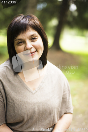 Image of mature brunette fat woman in green garden, smiling, friendly wel