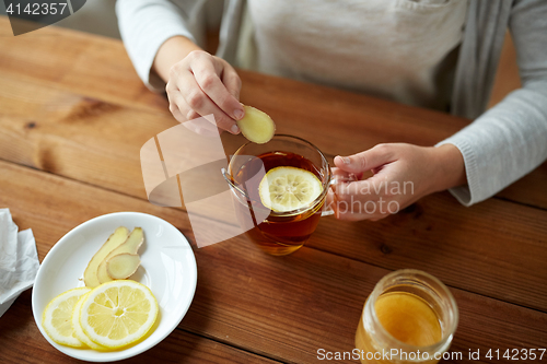 Image of close up of woman adding ginger to tea with lemon