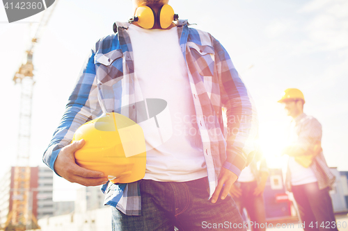 Image of close up of builder holding hardhat at building