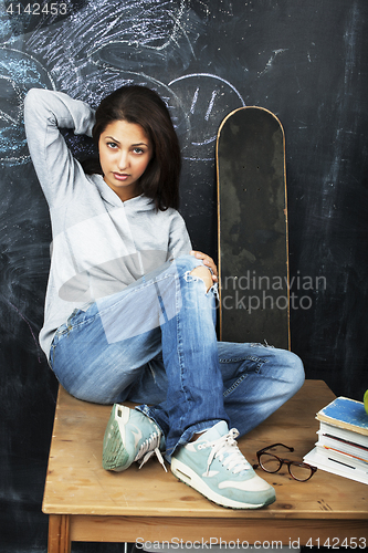 Image of young cute teenage girl in classroom at blackboard seating on ta