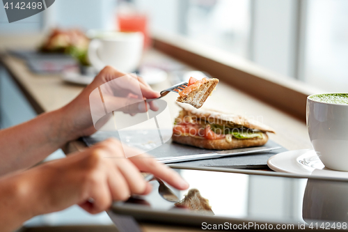 Image of woman with tablet pc and panini sandwich at cafe