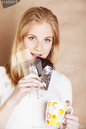 Image of young cute blond girl eating chocolate and drinking coffee close