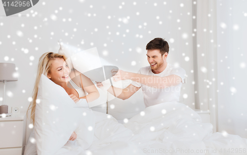 Image of happy couple having pillow fight in bed at home