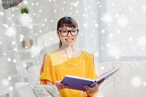 Image of smiling young asian woman reading book at home